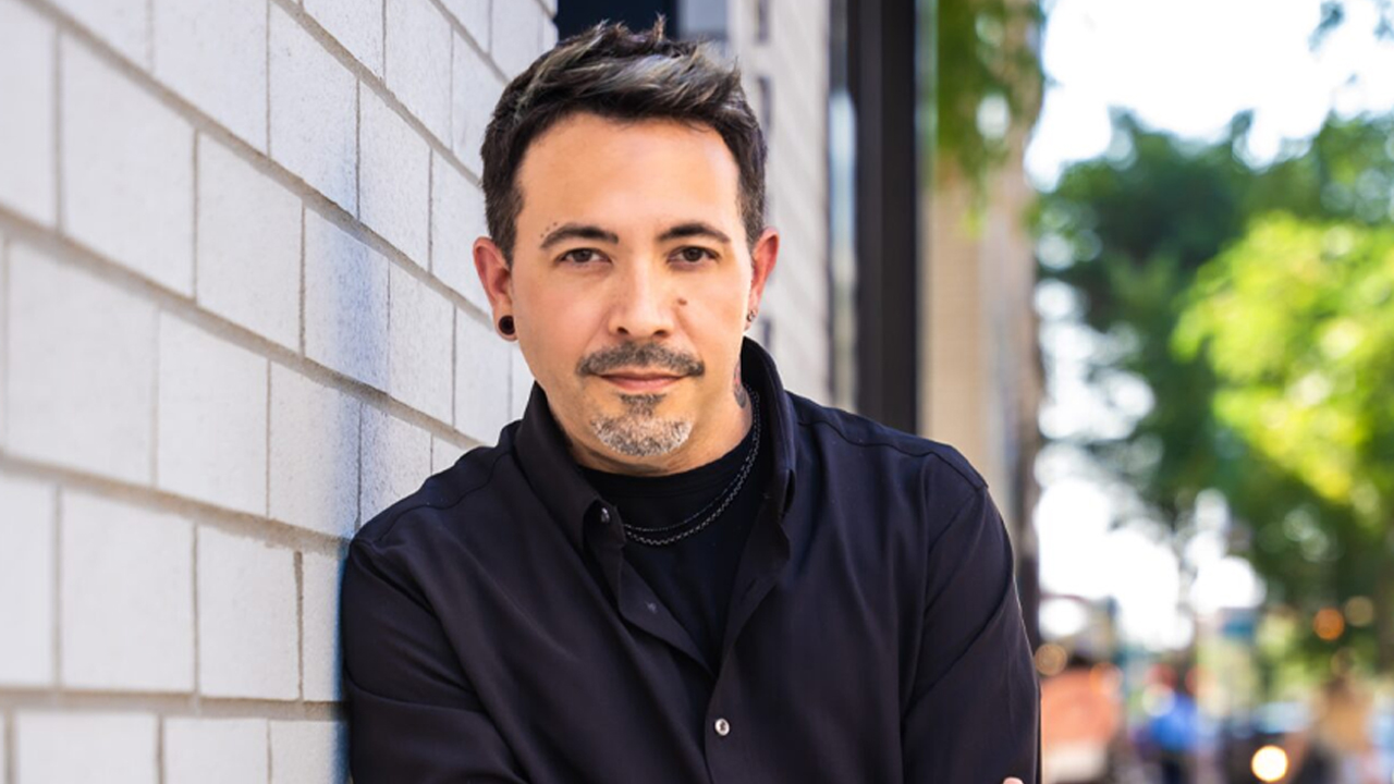 Celebrity Master Stylist Eli Mancha smiling in a modern salon, holding the Chicago Reader Best Hairdresser 2024 award, surrounded by stylists at Bang! Salon in Wicker Park.